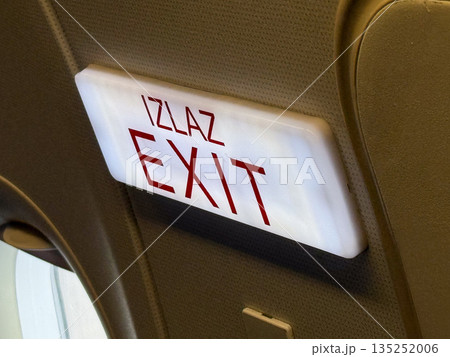 Airplane exit sign with bilingual marking. Safety, navigation, and emergency direction inside passenger aircraft. 135252006