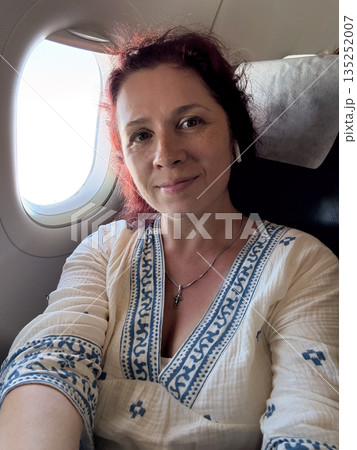 Passenger woman looking through airplane window during flight. Travel, contemplation, and personal experience of air journey. 135252007