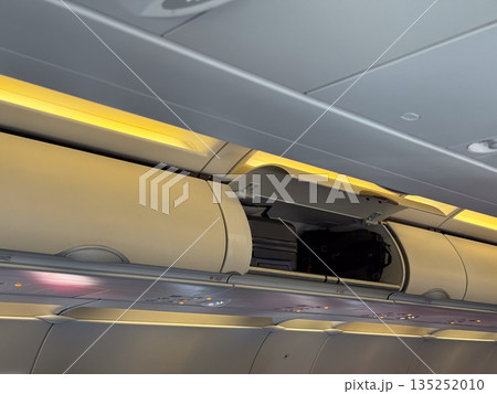 Overhead storage bins inside airplane cabin with luggage and personal items secured for travel. Aviation, mobility, and tourism lifestyle highlighting preparation, safety, and passenger journey. 135252010