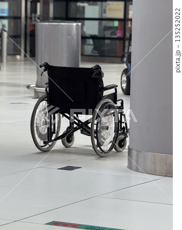 Empty wheelchair placed near column inside airport terminal hall. Mobility assistance availability, accessibility awareness, inclusive transport services, and support infrastructure concept. Empty wheelchair placed near column inside airport terminal hall. Mobility assistance availability, accessibility awareness, inclusive transport services, and support infrastructure concept. 135252022