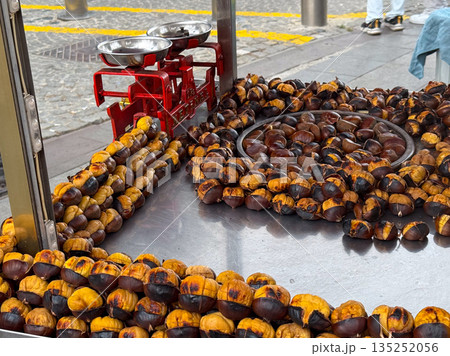 Roasted chestnuts arranged on a metal tray at a street food stand. Seasonal street cuisine, traditional roasting methods, and warm comfort food associated with autumn markets. 135252056