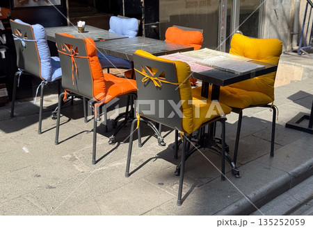 Outdoor cafe with chairs and tables, and bright yellow and red pillows. Hospitality, comfort, and lifestyle in an urban social setting. Outdoor cafe with chairs and tables, and bright yellow and red pillows. Hospitality, comfort, and lifestyle in an urban social setting. 135252059