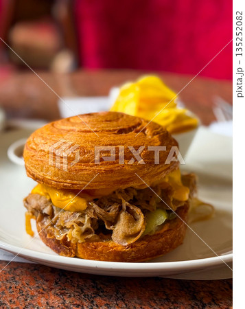 Croissant sandwich with meat and melted cheese served on a plate in a cozy cafe close-up. Gastronomy, lifestyle, and casual dining experience with comfort and indulgence. Croissant sandwich with meat and melted cheese served on a plate in a cozy cafe close-up. Gastronomy, lifestyle, and casual dining experience with comfort and indulgence. 135252082