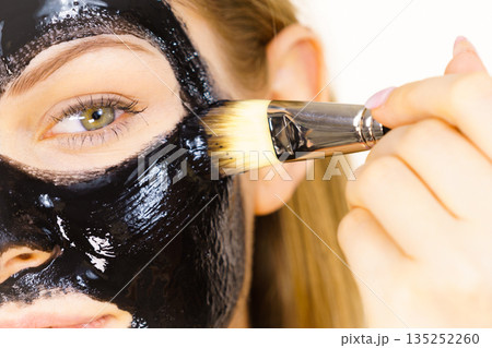 Woman applying black mud mask to face Woman applying black mud mask to face 135252260