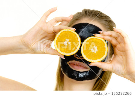 Girl black carbo mask on face holds orange fruit 135252266
