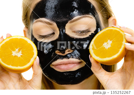 Girl black carbo mask on face holds orange fruit 135252267