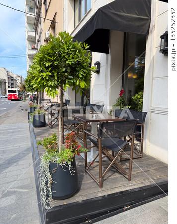 Outdoor cafe terrace with tables and chairs along a city sidewalk. Urban dining, street hospitality, and relaxed European cafe lifestyle Outdoor cafe terrace with tables and chairs along a city sidewalk. Urban dining, street hospitality, and relaxed European cafe lifestyle 135252352