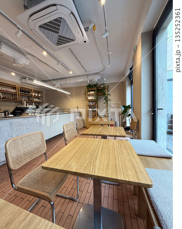 Modern cafe interior with wooden tables and woven chairs near window. Minimal design, natural materials, and cozy urban atmosphere 135252361