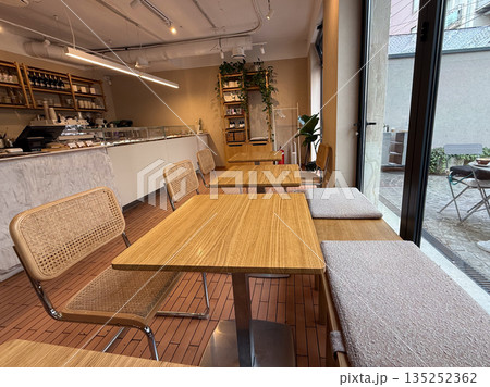 Modern cafe interior with wooden tables and woven chairs near window. Minimal design, natural materials, and cozy urban atmosphere 135252362