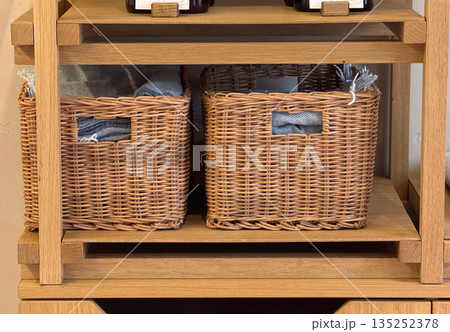 Wicker storage baskets on wooden shelving with folded fabric inside. Home organization, interior storage, and natural material decor for modern living Wicker storage baskets on wooden shelving with folded fabric inside. Home organization, interior storage, and natural material decor for modern living 135252378