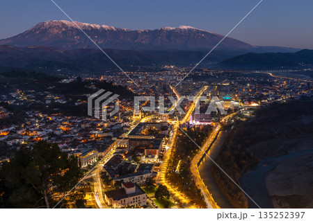 Night cityscape with modern residential buildings, illuminated streets, dense urban center and snow mpuntains peaks, Berat, Albania Night cityscape with modern residential buildings, illuminated streets, dense urban center and snow mpuntains peaks, Berat, Albania 135252397