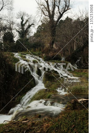 Small cascading streams of Kravica Waterfall flowing over mossy rocks and dense vegetation in Bosnia and Herzegovina. Natural wilderness scene with wet textures and flowing water 135253008