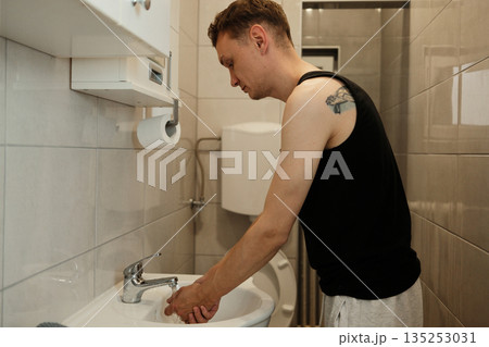 A man washes his hands in a small bathroom sink. The concept highlights hygiene and daily routine 135253031