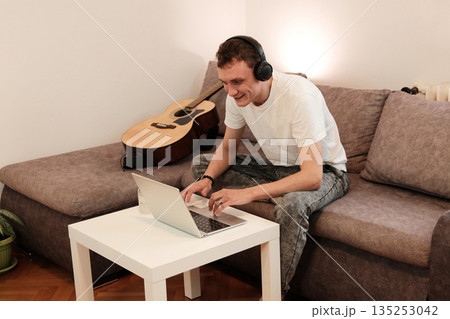 A man works on his laptop while sitting on the sofa. The concept reflects productivity and remote work in a relaxed home environment 135253042