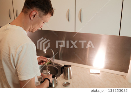 A man scoops ground coffee into a moka pot in the kitchen. The moment highlights a peaceful home routine concept A man scoops ground coffee into a moka pot in the kitchen. The moment highlights a peaceful home routine concept 135253085