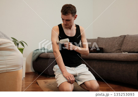 A man applies a massage gun to his arm while kneeling on the floor. The moment illustrates muscle recovery concept A man applies a massage gun to his arm while kneeling on the floor. The moment illustrates muscle recovery concept 135253093