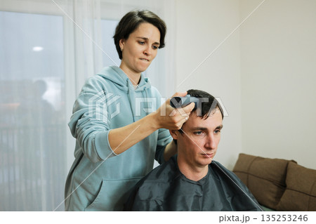 A woman uses a trimmer to shorten a man s hair during a home haircut. The moment reflects personal grooming and the concept of everyday care A woman uses a trimmer to shorten a man s hair during a home haircut. The moment reflects personal grooming and the concept of everyday care 135253246