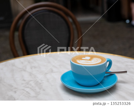 Heart-shaped latte art in a blue ceramic cup on a marble cafe table. A cozy outdoor coffee moment with elegant details and warm ambiance Heart-shaped latte art in a blue ceramic cup on a marble cafe table. A cozy outdoor coffee moment with elegant details and warm ambiance 135253326
