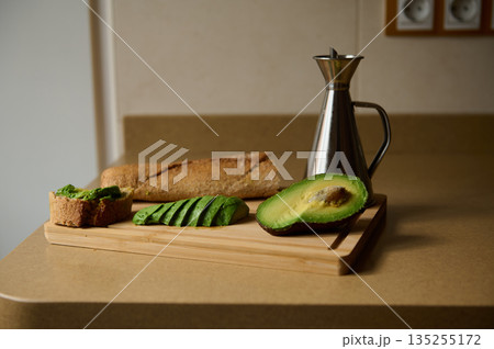 Avocado Slices With Whole Grain Bread On Cutting Board And Oil Bottle In Kitchen Scene 135255172