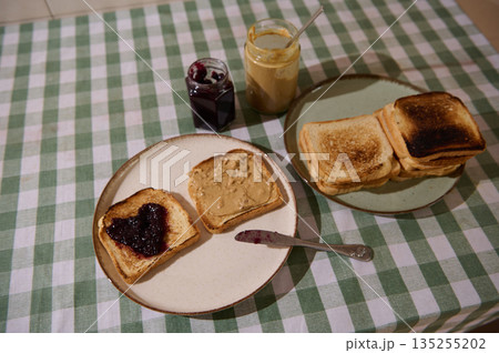 Family Breakfast Spread With Toast, Jam, And Peanut Butter On Checkered Tablecloth Family Breakfast Spread With Toast, Jam, And Peanut Butter On Checkered Tablecloth 135255202