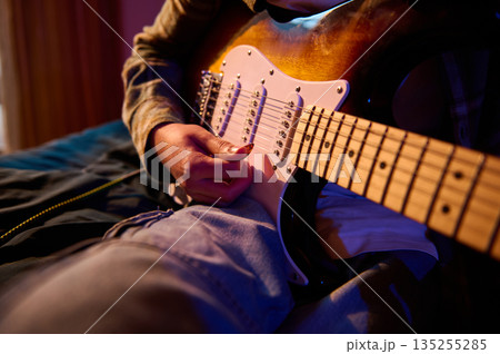 Close-Up Of Person Playing Electric Guitar In Bed With Warm Ambient Lighting Close-Up Of Person Playing Electric Guitar In Bed With Warm Ambient Lighting 135255285