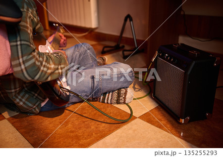 Person Playing Electric Guitar at Home With Amplifier in Cozy Music Room 135255293