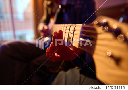 Close-Up Of Hands Playing Guitar With Focus On Frets And Strings In A Cozy Room Close-Up Of Hands Playing Guitar With Focus On Frets And Strings In A Cozy Room 135255316