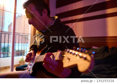 Man Playing Electric Guitar In Cozy Room With Sunset Light On Balcony Man Playing Electric Guitar In Cozy Room With Sunset Light On Balcony 135255318