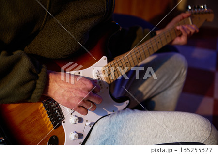 Close-Up Of Player Strumming An Electric Guitar In A Cozy Indoor Setting Close-Up Of Player Strumming An Electric Guitar In A Cozy Indoor Setting 135255327