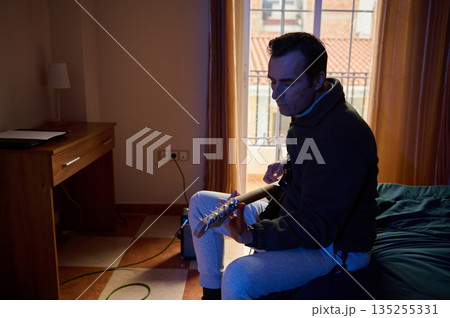 Man Playing Electric Guitar Indoors In Cozy Hotel Room With Curtains And Bed Man Playing Electric Guitar Indoors In Cozy Hotel Room With Curtains And Bed 135255331