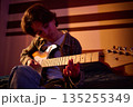 Young Guitarist Plays Electric Guitar in Warm Dimly Lit Room 135255349