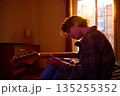 Young guitarist Sitting Indoors In Plaid Shirt As Sunset Light Falls On Warm Room 135255352