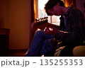 Young Man Playing Acoustic Guitar At Home In Warm Evening Light, Cozy Room Mood 135255353