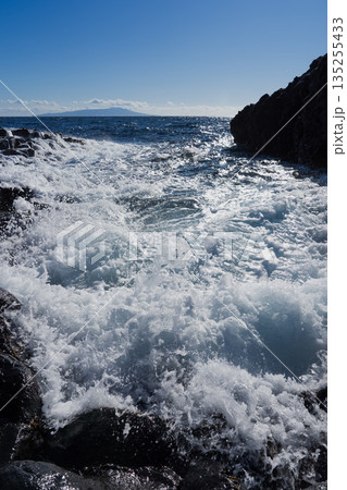 岩礁に寄せる波と遠景に浮かぶ島のある海 岩礁に寄せる波と遠景に浮かぶ島のある海 135255433