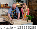 Generations unite in kitchen during heartfelt baking session, Tender moment as grandfather guides granddaughter through traditional baking techniques in warm home 135256289