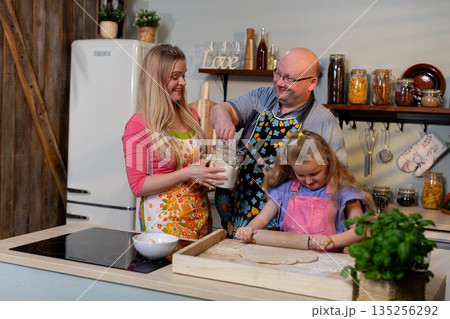 Family bakes joyfully, Parents and daughter rejoice over freshly baked homemade bread, Cheerful family celebrates their success in baking bread together in cozy kitchen 135256292