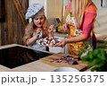 Girl tries dessert with mother, Child explores homemade sweets with guiding parent nearby, Young girl in chef hat enjoying homemade dessert while mother supervises closely 135256375