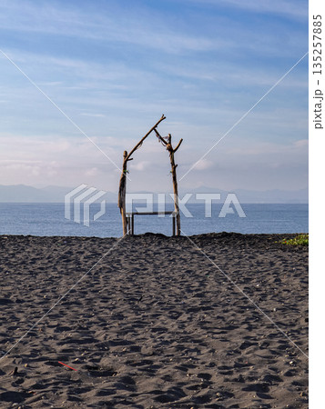 Rustic driftwood archway on black sand beach at sunrise with natural light, offering a tranquil escape and a unique coastal experience in Bali, Indonesia 135257885