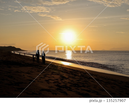 Silhouette of family enjoying a sunset walk on the beach with golden light reflecting on the water for a tranquil vacation moment 135257907