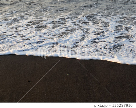 Ocean Waves Washing Ashore on Black Sand Beach with Natural Light creating a serene coastal scene for travel and relaxation 135257910