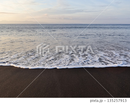Serene ocean waves washing onto black sand beach with natural light, creating calming atmosphere for coastal vacation and travel themes Serene ocean waves washing onto black sand beach with natural light, creating calming atmosphere for coastal vacation and travel themes 135257913