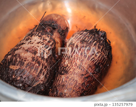 Close-up of boiled taro roots in a metallic pot, highlighting their rough texture and dark brown color, perfect for culinary blogs and cooking tutorials 135257979