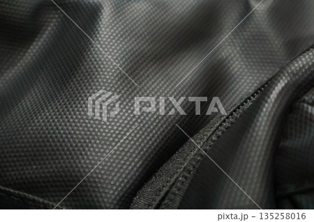 Close-up of dark nylon fabric with a textured surface and zipper, showcasing durability and modern design for versatile applications Close-up of dark nylon fabric with a textured surface and zipper, showcasing durability and modern design for versatile applications 135258016