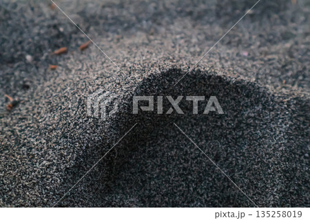 Close-up of textured dark gray sand forming a small dune with shadows, creating an abstract natural background for environmental science use 135258019