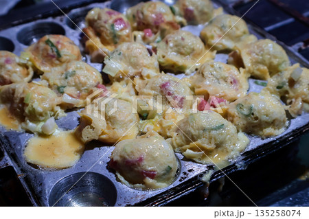 Delicious Takoyaki Cooking in a Pan with Natural Light, Close-Up View of Japanese Octopus Balls Being Prepared for Street Food Vending Delicious Takoyaki Cooking in a Pan with Natural Light, Close-Up View of Japanese Octopus Balls Being Prepared for Street Food Vending 135258074