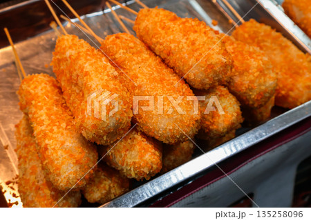 Pile of corn dogs displayed in a tray, coated with crispy orange breading under natural light, perfect for showcasing street food or fair snacks Pile of corn dogs displayed in a tray, coated with crispy orange breading under natural light, perfect for showcasing street food or fair snacks 135258096