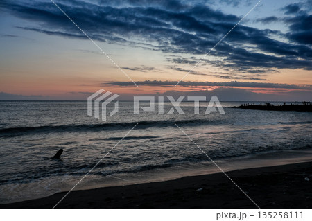 Calm ocean sunset with dramatic clouds reflecting soft natural light on rippled sea, creating a serene and peaceful coastal landscape for relaxation 135258111