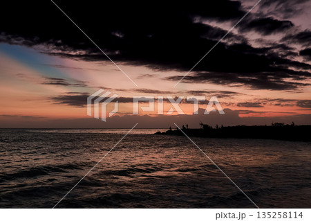 Ocean Sunset with Dark Clouds: Silhouette of Land with People enjoying golden hour, captured in natural light for coastal serenity 135258114