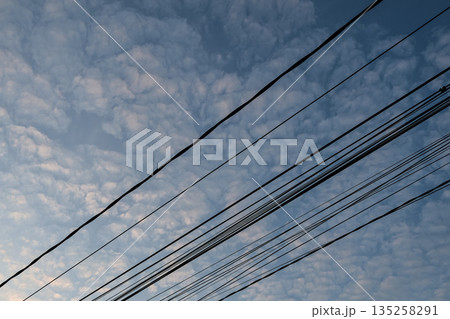 Overhead power lines crossing sky with clouds, natural light casting a soft glow for energy and infrastructure visuals Overhead power lines crossing sky with clouds, natural light casting a soft glow for energy and infrastructure visuals 135258291