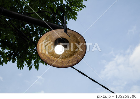 Outdoor light fixture hanging with natural light and copy space on a partly cloudy sky background, perfect for architectural or design projects. Outdoor light fixture hanging with natural light and copy space on a partly cloudy sky background, perfect for architectural or design projects. 135258300